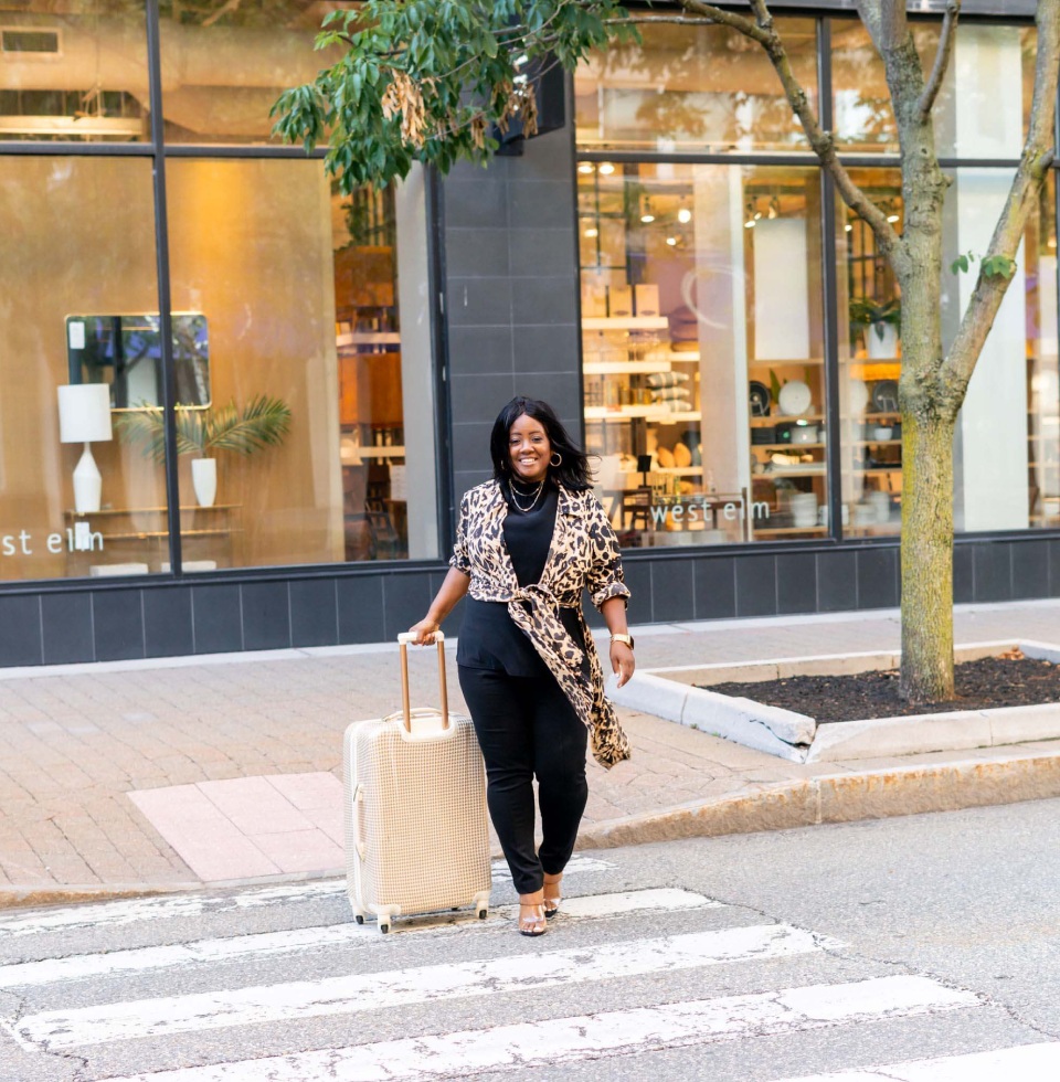 A woman is crossing the street with her luggage.