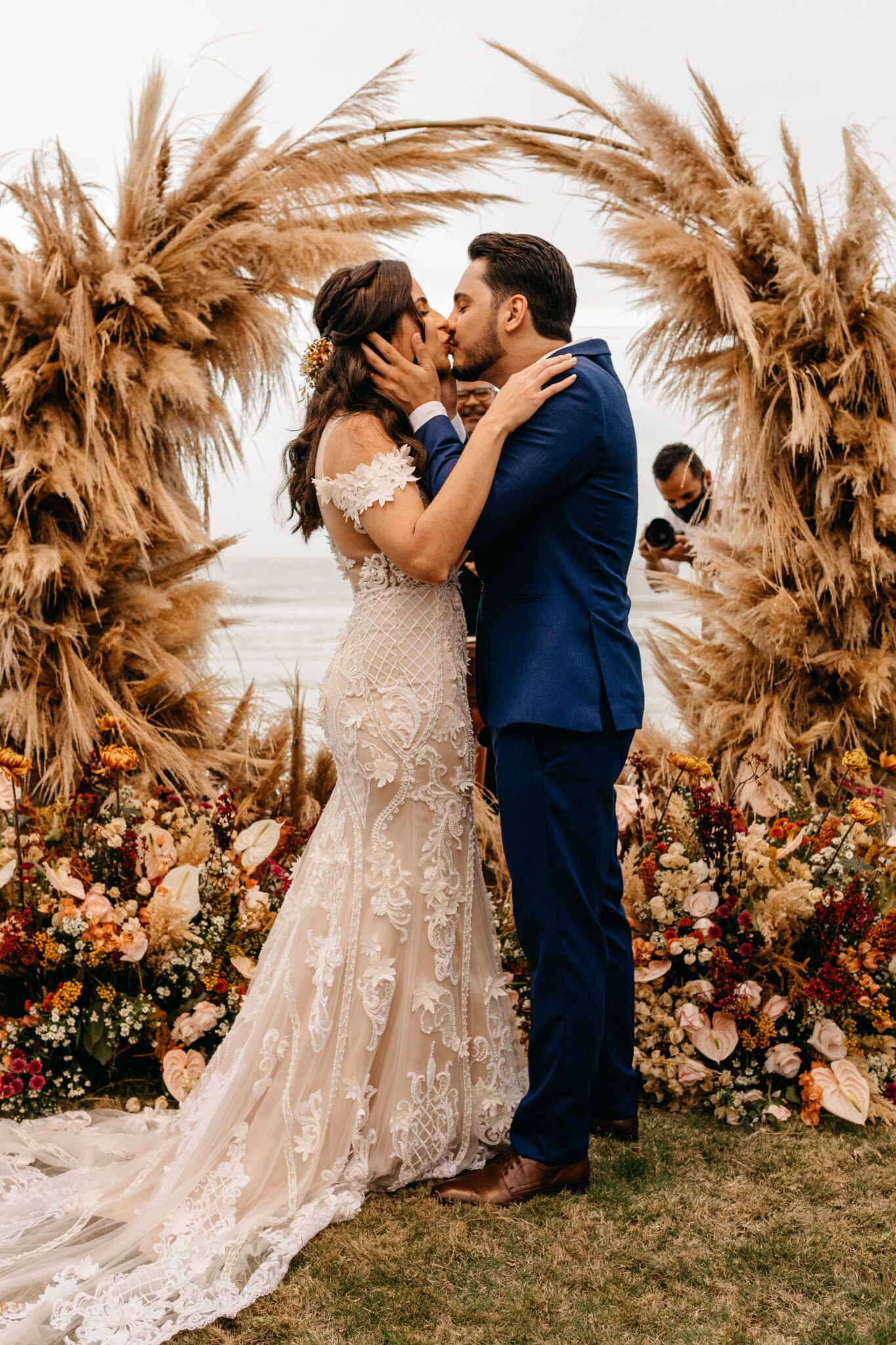 A couple kissing in front of an arch made out of flowers.