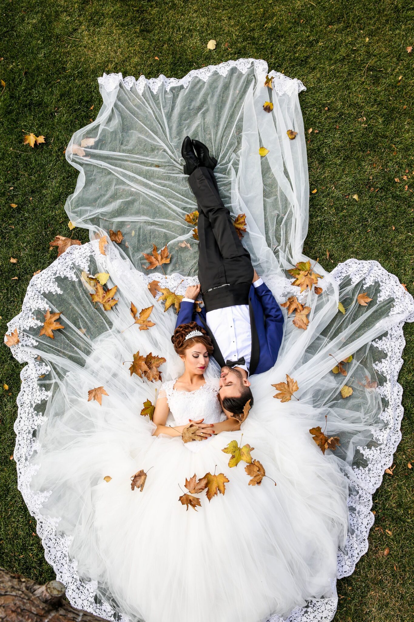 A man and woman laying on the ground in wedding attire.